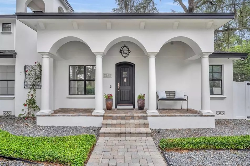 Close view of the front porch at 221 Minnehaha: three arched openings supported by classical columns, a dark wood front door, a paver walkway, and a teak bench under the colonnade