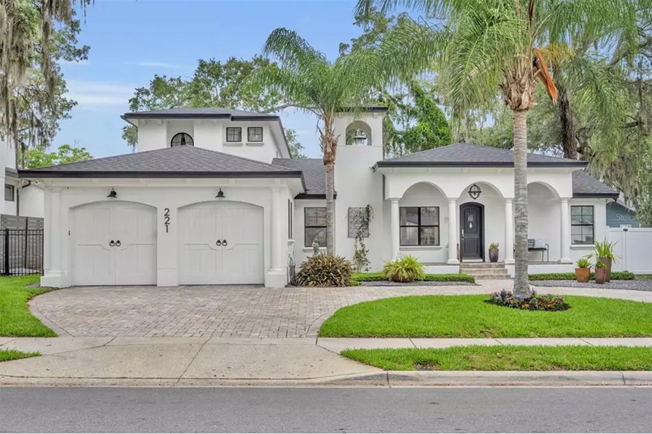The white stucco facade and arched colonnade entry of 221 Minnehaha, framed by mature palms and a paver circular drive
